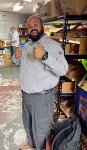 A happy man giving thumbs up in the storage room of the plumbing company building.